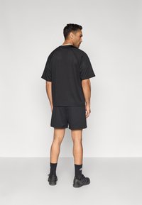 Μαύρο αθλητικό σύνολο με κοντομάνικη, αεριζόμενη μπλούζα και ταίριαστα σορτς. Φοριέται με μαύρα παπούτσια και κάλτσες. Μινιμαλιστικός σχεδιασμός.