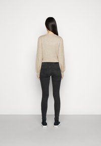 Sweater de malha bege com mangas bufantes, combinado com jeans pretos ajustados e ténis pretos. O fundo é branco liso.