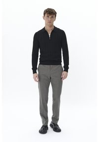 Camisa polo de manga larga negra con un cuello con cremallera, combinada con pantalones grises a cuadros y zapatos negros con cordones. Diseño minimalista, estilo ajustado.