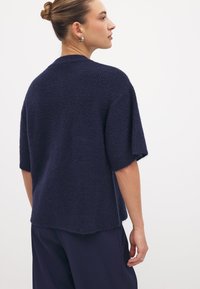 Donkerblauwe gebreide trui met korte mouwen, met een textuurafwerking en een relaxte pasvorm, afgewerkt met een licht ongelijke zoom.