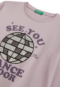 Světle fialové tričko s flitrovou diskovou koulí a fialovým textem "UVIDÍME SE NA TANEČNÍM PARKETU" a zelenou etiketou "United Colors of Benetton."
