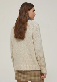 Maglione crema spesso con lavorazione a maglia testurizzata, orlo a coste e sottili accenti scintillanti sulle maniche. Abbinato a una gonna a quadri.