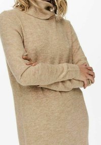 Pull à col roulé beige avec un tricot doux et texturé. Comprend des manches longues et une coupe confortable, s'étendant jusqu'à mi-cuisse.