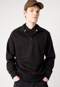 Maglione nero a mezza zip con un motivo a maglia testurizzato, polsini a costine e colletto pieghevole con sottili accenti di colore.
