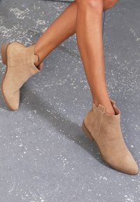 Botines de ante en color beige con detalles de costura, punta afilada y un tacón bajo apilado. Idóneos para un estilo casual.
