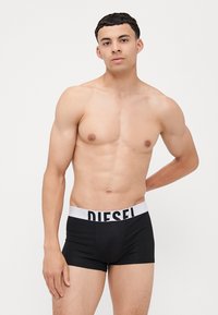 Boxer briefs neri da uomo con un elastico bianco che presenta la scritta "DIESEL" stampata sul davanti. Tessuto morbido e vestibilità aderente. Modello in posa in piedi.