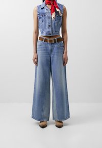 Džínový zkrácený vest v světle modré barvě, kombinovaný s volnými světle modrými džíny. Hnědý opasek a červený šátek pro akcent. Hladká textura, ležérní design.