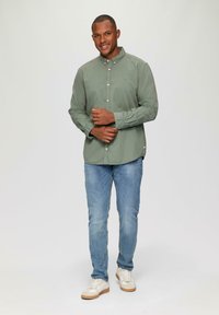 Een lichtgroene katoenen overhemden met knopen, gecombineerd met lichtblauwe jeans. De outfit wordt aangevuld met witte sneakers met een gestructureerde zool.
