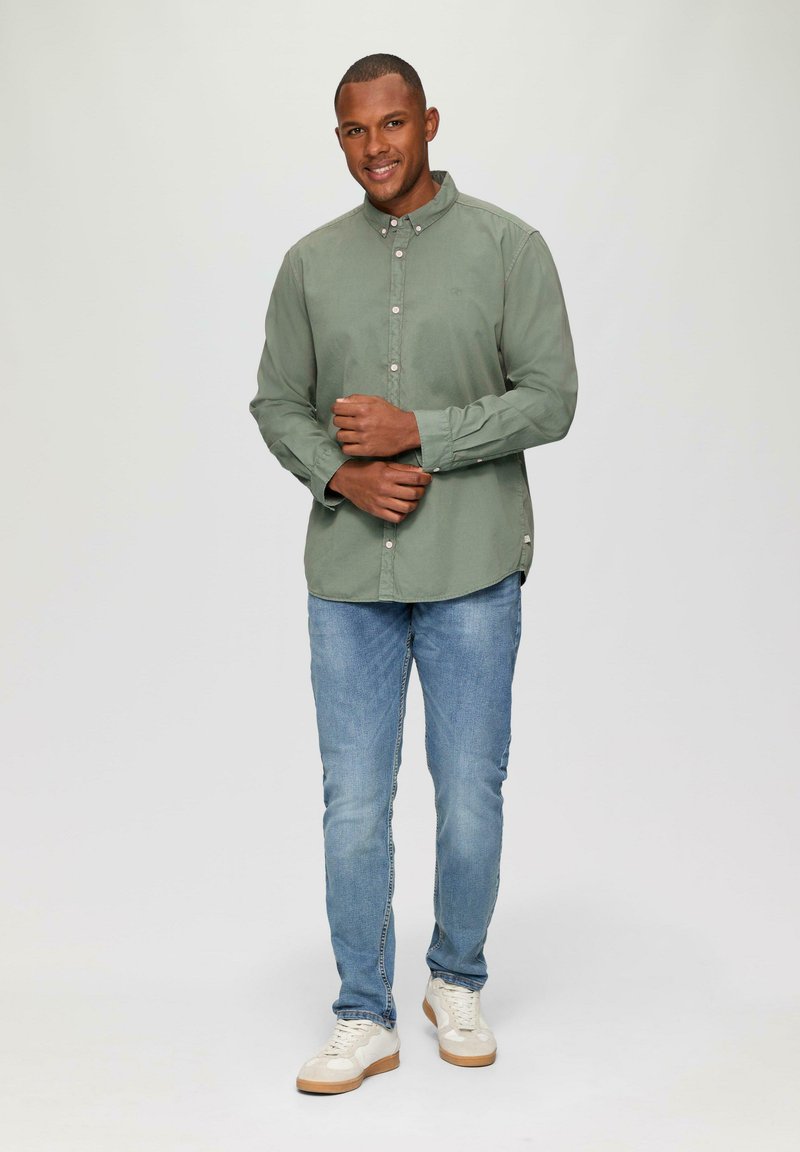 Een lichtgroene katoenen overhemden met knopen, gecombineerd met lichtblauwe jeans. De outfit wordt aangevuld met witte sneakers met een gestructureerde zool.