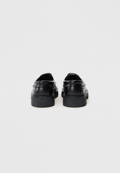Et par sorte læder loafers med kraftige såler, set fra bagved på en almindelig hvid baggrund.