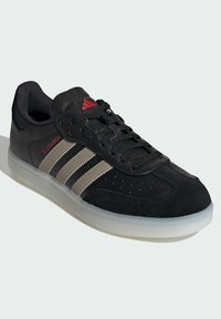 Czarne buty sportowe z zamszowej i syntetycznej cholewki, trzy srebrne paski, perforowane detale, czarne sznurowadła i biała gumowa podeszwa.