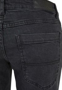 Jeans in denim nero con una texture liscia, dotati di una tasca posteriore, cuciture rinforzate e un'etichetta in pelle sul cinturino.
