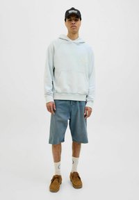 Light blue hoodie with kangaroo pocket, denim shorts, tan shoes, and white socks featuring a logo. Stands on a neutral background.