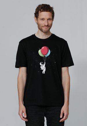 Zwart katoenen T-shirt met een grafische afbeelding van een astronaut die kleurrijke ballonnen vasthoudt, met een sterrenacht achtergrond. Korte mouwen.