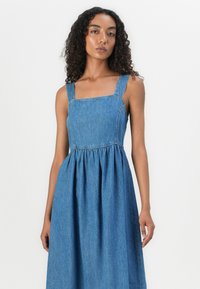 Denim dress with a square neckline, thick straps, gathered waist, and a flared skirt, showcasing a medium blue color with a smooth texture.