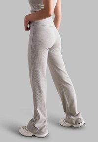 Jasnoszare, prążkowane spodnie sportowe z rozszerzanymi nogawkami, z szerokim pasem i gładką fakturą. Noszone z białymi butami sportowymi.