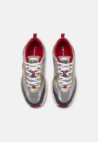 Lacoste sneakers featuring a silver mesh upper with gold and black accents, red interior, white laces, and a textured outsole.