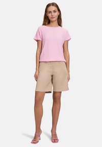 Haut rose clair texturé à manches courtes associé à un short beige丈. Le modèle porte également des sandales roses à lanières. Design minimaliste.