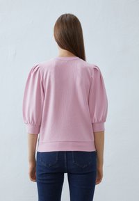 Růžová mikina s nafouknutými rukávy, žebrovanými manžetami a lemem. Hladká texturu, ležérní design, doplněná modrými přiléhavými džíny.