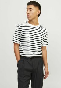 Hvid t-shirt med korte ærmer og sorte vandrette striber, parret med sorte bukser og et vævet bælte. Enkel, klassisk design.