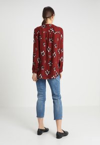 Camicia a maniche lunghe rossa con fiori e righe verticali, con motivi di fiori bianchi e neri, abbinata a jeans azzurri corti e ballerine nere.
