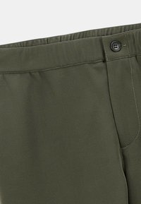 Pantalons vert olive avec une taille élastique, fermeture à un bouton et détails de couture contrastants sur les coutures.