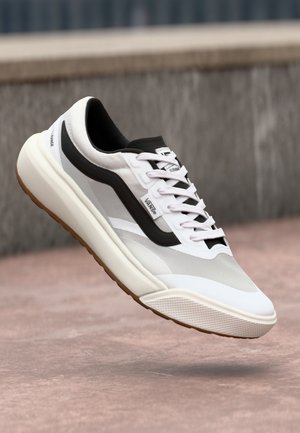 White and black sneaker with a textured design, suspended above a light-colored surface, showcasing its modern style and details.