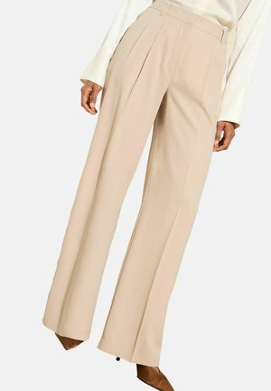 Beige wijde broek van gladde stof, met persplooien en een hoge taille. Draagt bij puntige enkelboots.
