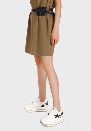 Sneakers platform bianchi con accenti a stella nera e dettagli maculati marroni. Abbinate a un vestito color khaki e una cintura nera con borsellino.