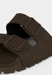Gros plan d'une sandale marron avec deux sangles réglables à boucles et une semelle texturée pour l'adhérence et le confort.