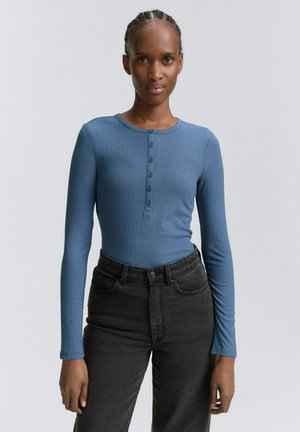 Langsleeve blauwe geribbelde top met een ronde halslijn en een knoopsluiting met vijf knopen, gecombineerd met zwarte high-waisted jeans. Gladde textuur, aansluitend ontwerp.