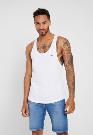 White cotton tank top with round neckline, featuring a small "Lee" logo and paired with blue denim shorts. Model has visible tattoos.