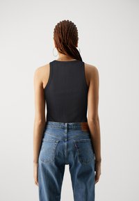 Svart ribbestrikket tanktop kombinert med blå høyhåndsjeans, med klassisk søm på baklommene og et lær merke.