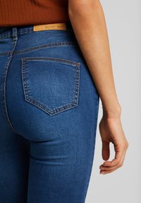 Jeans de mezclilla azul ajustados con una textura suave, que presentan un bolsillo trasero rectangular y una etiqueta que dice "NOISY MAY" en la cinturilla.