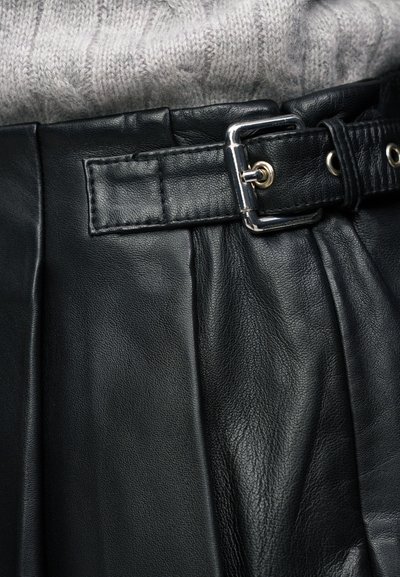 Ceinture noire en cuir avec boucle argentée attachée autour d'une jupe en cuir noir, associée à un pull en maille gris clair.