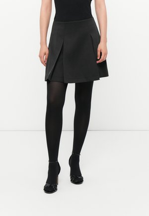 Black A-line skirt with pleats, paired with black tights and open-toed heels; smooth fabric with a structured design and layered appearance.