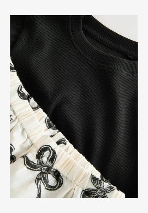 Fekete bordázott felső, krémszínű anyagú alsó résszel, fekete masni mintával. A felső kerek nyakú, az alsó rész ráncolt.