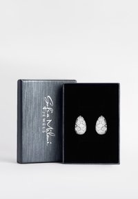 Silver droppformade örhängen med ett vadderat mönster, placerade i en svart sammetsfållad låda med en metallisk blå utsida.