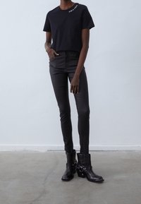 T-shirt noir en coton avec un petit motif blanc, associé à un pantalon noir ajusté et des bottines à la cheville avec un détail de boucle.