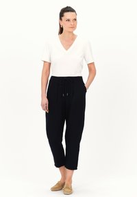 Marineblauwe broek met een trekkoord in de taille, twee voortassen, gecombineerd met een witte V-hals t-shirt. Model draagt beige suède moccasins.
