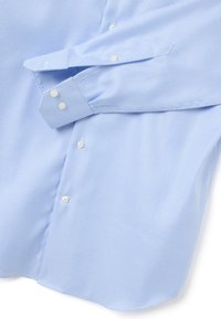 Camicia azzurra chiara con motivo a piccole righe, polsini con bottoni e bottoni bianchi, piegata con una manica sopra la parte frontale.