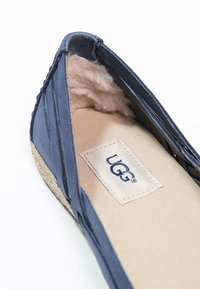 Marineblauwe UGG instapper met een zachte, fuzzy voering en een beige suède zool. Kenmerkt een geweven bovenkant en een zichtbaar logolabel aan de binnenkant.