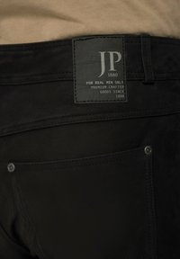 Schwarze Denim-Jeans mit einem Lederpatch mit "JP 1880" Branding, doppelt genähten Nähten und einer Gesäßtasche mit metallenen Nietenakzenten.
