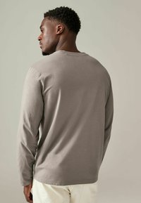 Grijze langetermijnshirt, gemaakt van zachte stof, met een ronde hals en een relaxed fit, van de achterkant weergegeven tegen een neutrale achtergrond.