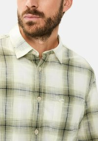 Hellgrünes kariertes Button-Down-Hemd mit weichem Textur, das dezente schwarze Linien aufweist und ein kleines gesticktes Logo auf der Brust hat.
