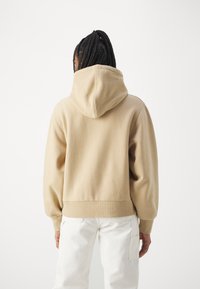 Beige hooded sweatshirt with a relaxed fit, ribbed cuffs and hem, and soft texture. Showcases a simple design without embellishments.
