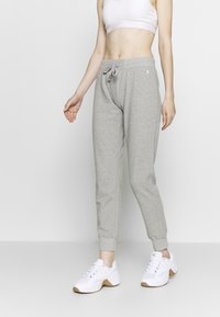 Gray sweatpants with a fitted design, drawstring waist, and elastic cuffs, paired with white athletic shoes. Smooth fabric texture.