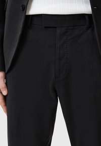 Black tailored trousers with a smooth texture, featuring a straight cut, front crease, and subtle side pockets, paired with a white sweater.