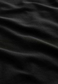 Schwarzer Stoff mit einer glatten Textur und weichen, fließenden Falten. Die Oberfläche wirkt leicht reflektierend, was auf eine synthetische Zusammensetzung hinweist.