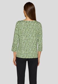 Grüner Kurzarm-Top mit schwarzen und blauen Leopardenflecken, runder Ausschnitt und lockerer Passform, kombiniert mit schwarzen Hosen.